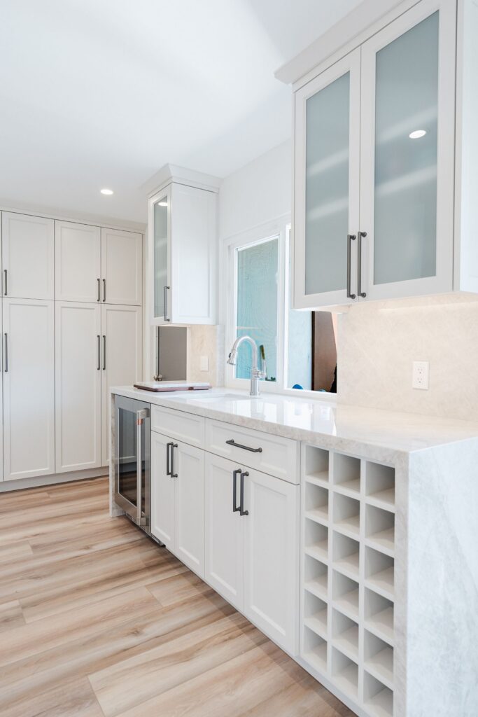 Kitchen storage wall with frosted-glass upper cabinets, beverage fridge, wine cubbies and waterfall stone counter.