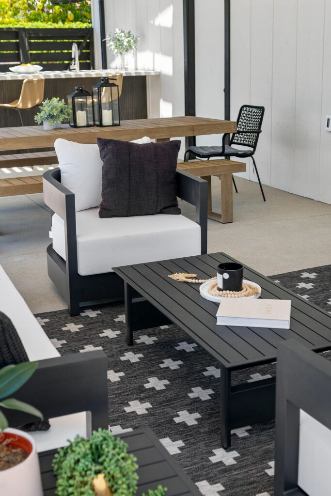 Outdoor lounge seating with black-and-white rug, dining table and kitchen bar beyond