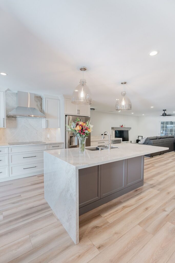 Dark paneled kitchen island with waterfall stone countertop, pendant lights and open connection to the living room.