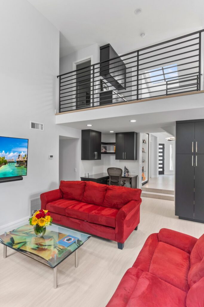 Family room with red sofas, built-in desk cabinetry, black loft railing and light wood-look flooring.