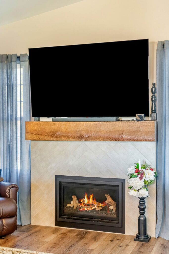 Living room fireplace with reclaimed wood mantle, herringbone tile surround and wall-mounted TV