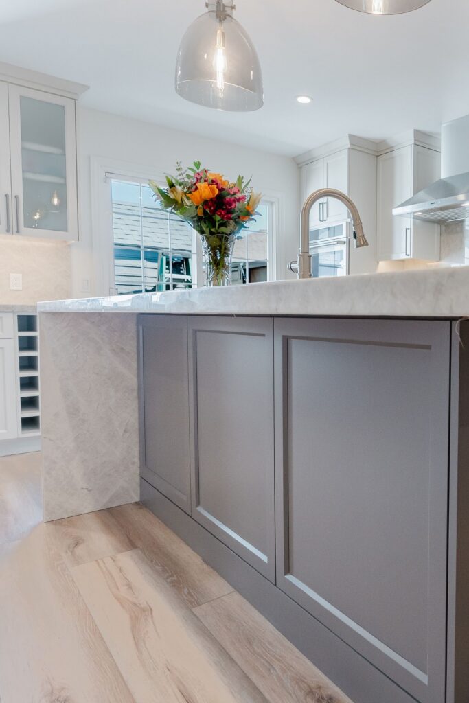 Dark kitchen island with waterfall stone counter and faucet, framed by white cabinetry and frosted-glass uppers.