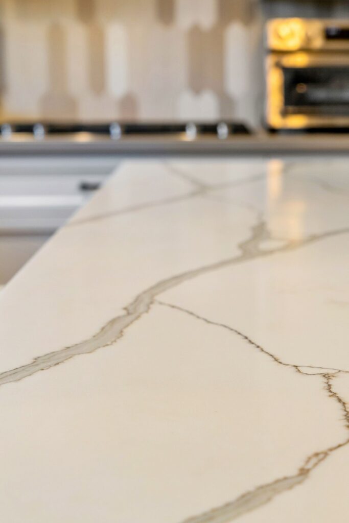 Close-up of quartz waterfall island countertop with veining and cooktop in background