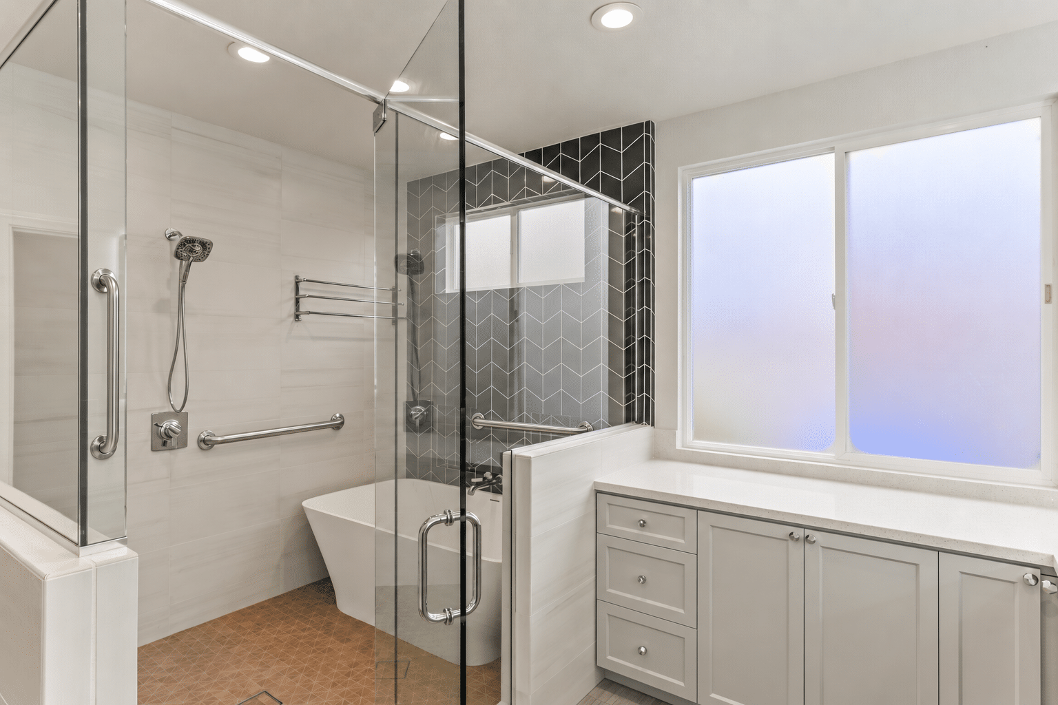 Accessible bathroom with a glass-enclosed shower, handheld showerhead, and stainless-steel grab bars installed along the shower walls.