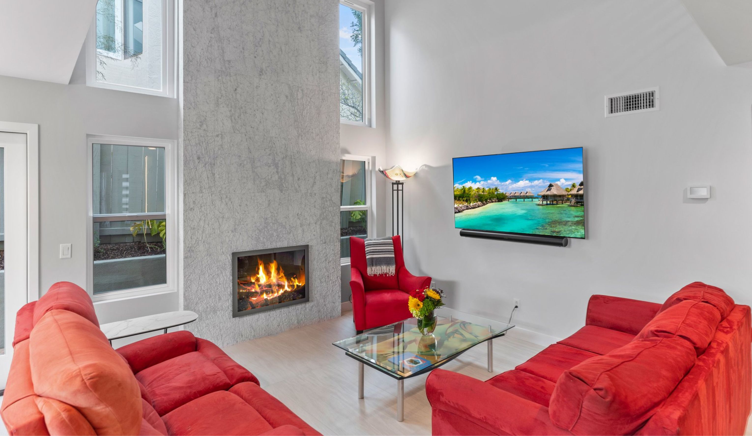 Rancho Peñasquitos living room remodel with floor-to-ceiling fireplace, tall windows, red seating and light wood flooring.