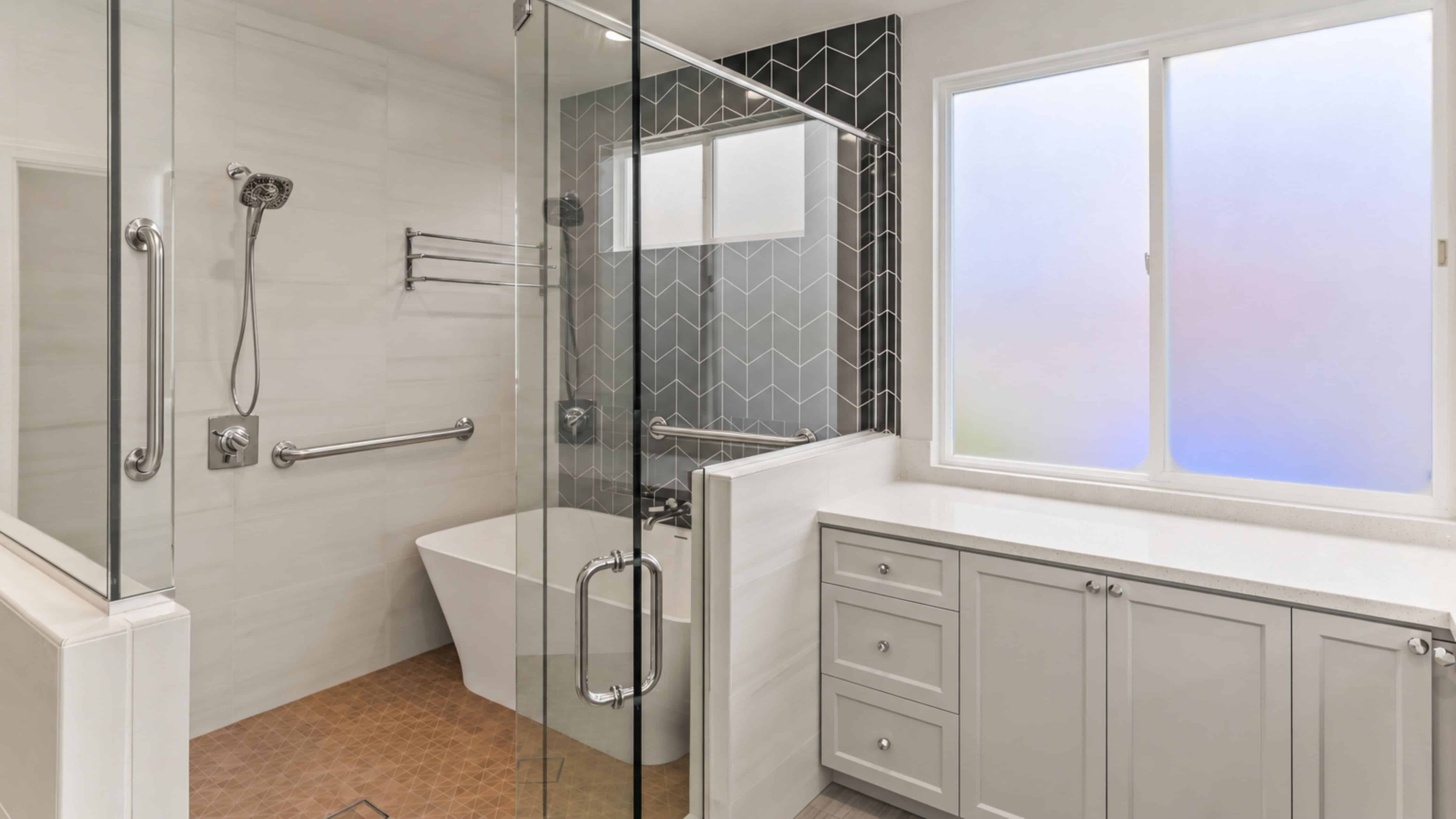 Spacious white primary bathroom with double vanity, round black-framed mirrors, freestanding soaking tub, and glass-enclosed herringbone tile shower.