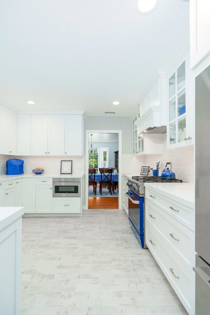White shaker kitchen with blue range, glass-front cabinets, quartz counters and light gray tile flooring