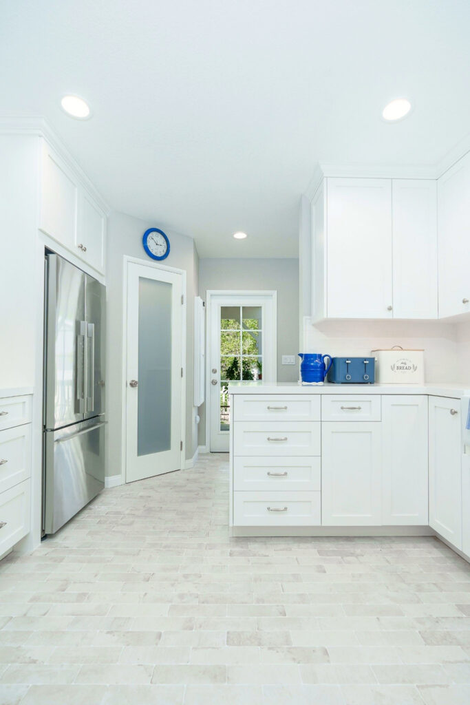 Kitchen with stainless refrigerator, frosted-glass pantry door, white shaker cabinetry and recessed lighting