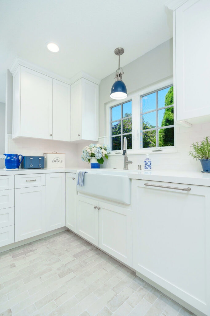 Corner kitchen sink area with white cabinetry, subway tile backsplash, quartz counters and blue pendant