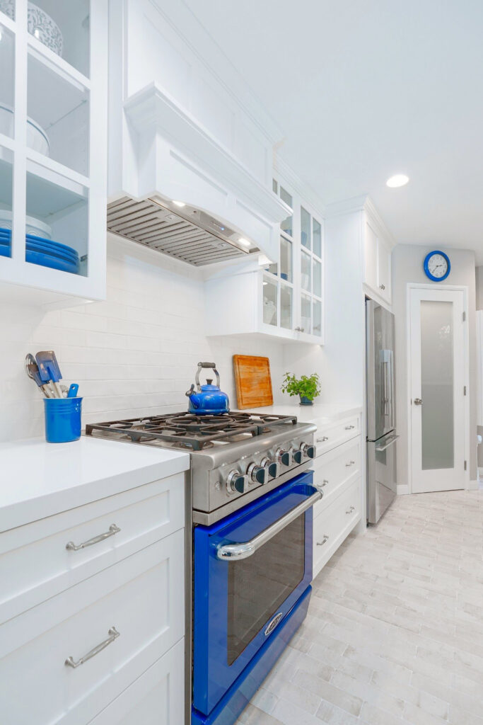 Blue range with custom hood, glass-front cabinets, white subway tile and stainless refrigerator