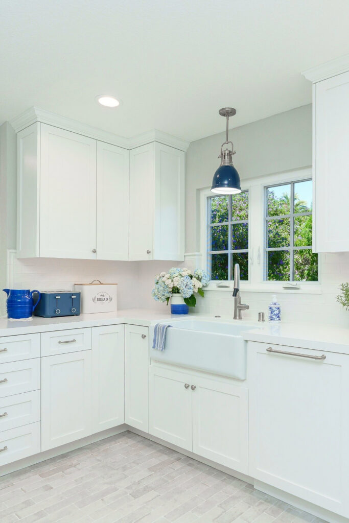 Farmhouse sink corner with white shaker cabinetry, quartz countertops, subway tile and blue pendant light