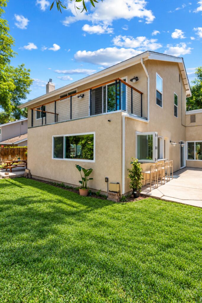 San Diego home addition with a cable-rail balcony above, a picture window and a bi-fold kitchen window with patio bar stools
