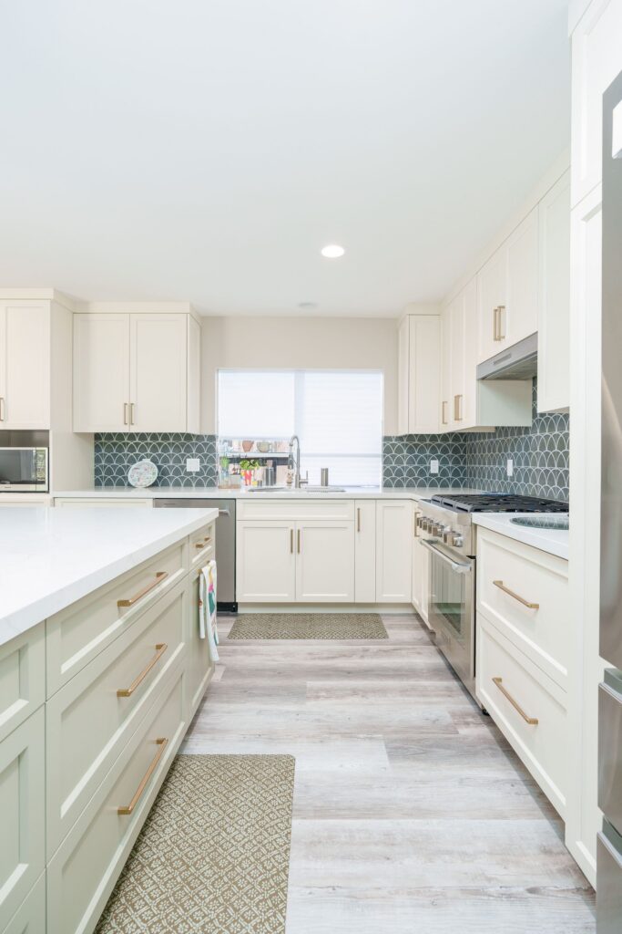 Galley view of San Diego kitchen remodel with sage green island drawers, cream shaker cabinets, fan tile backsplash and window
