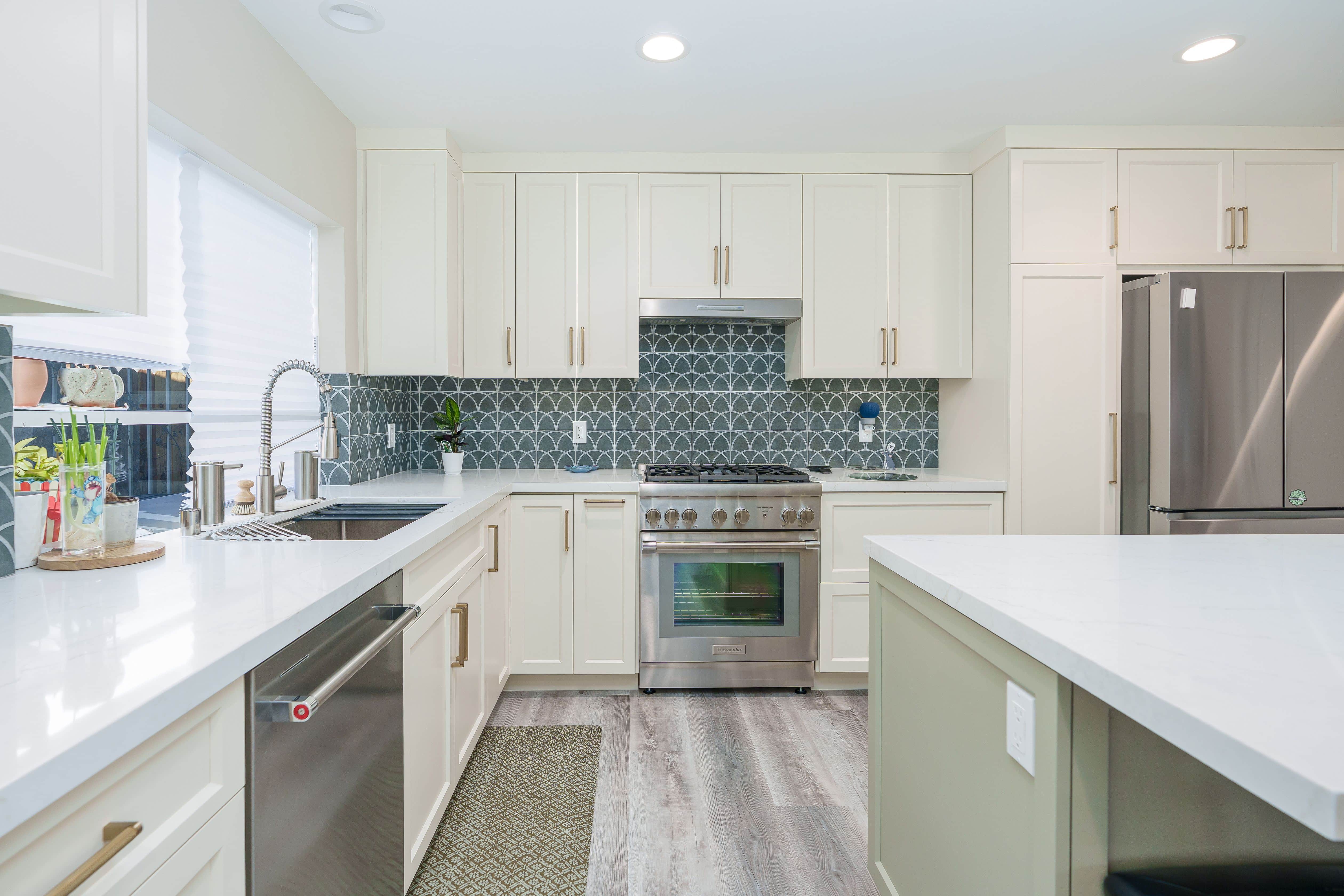 Kitchen with cream shaker cabinets, brass pulls, green fan-pattern tile backsplash, stainless range and white countertops