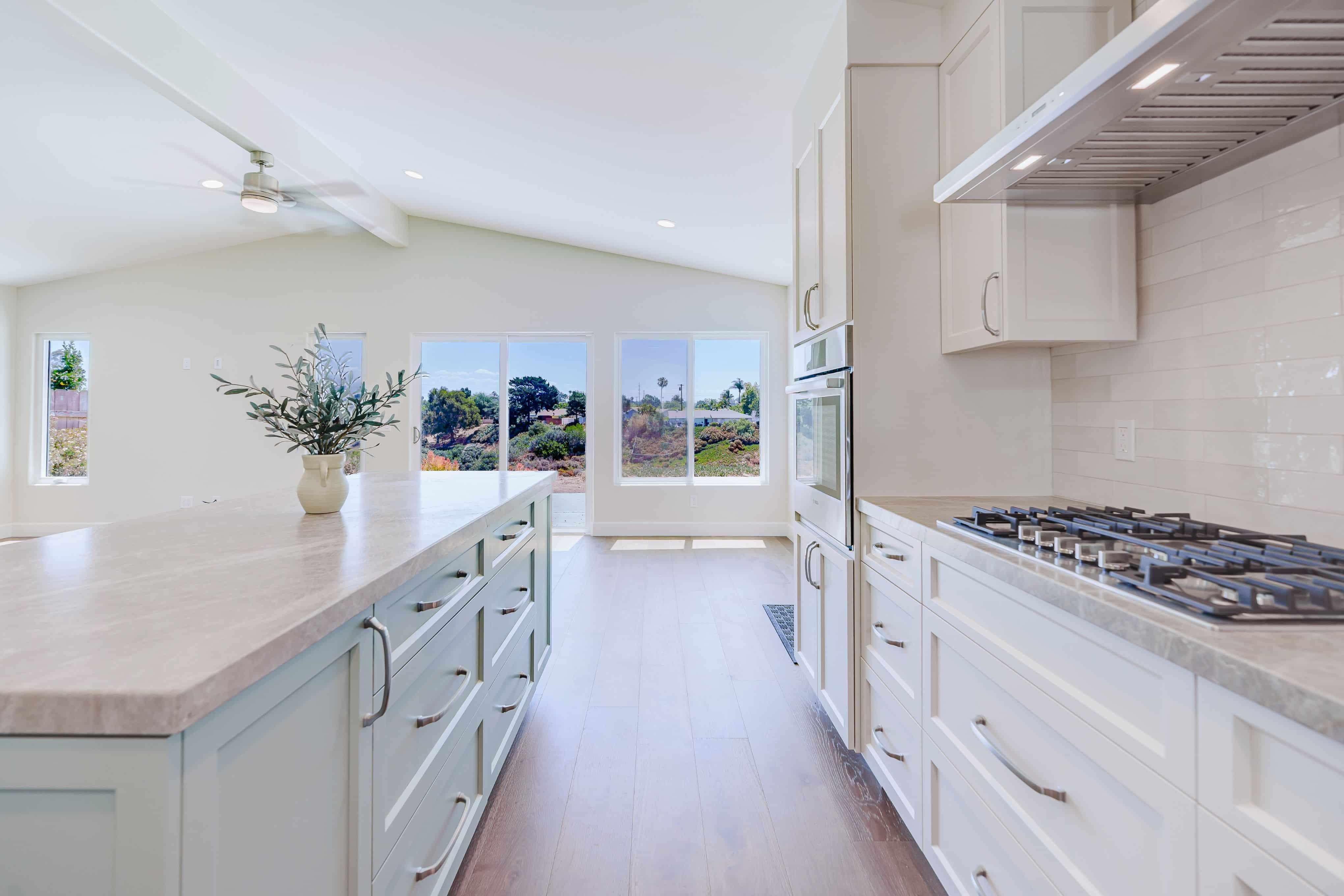 Open kitchen with sage green island, white Shaker cabinets, gas cooktop, wall oven and vaulted ceiling facing canyon-view windows
