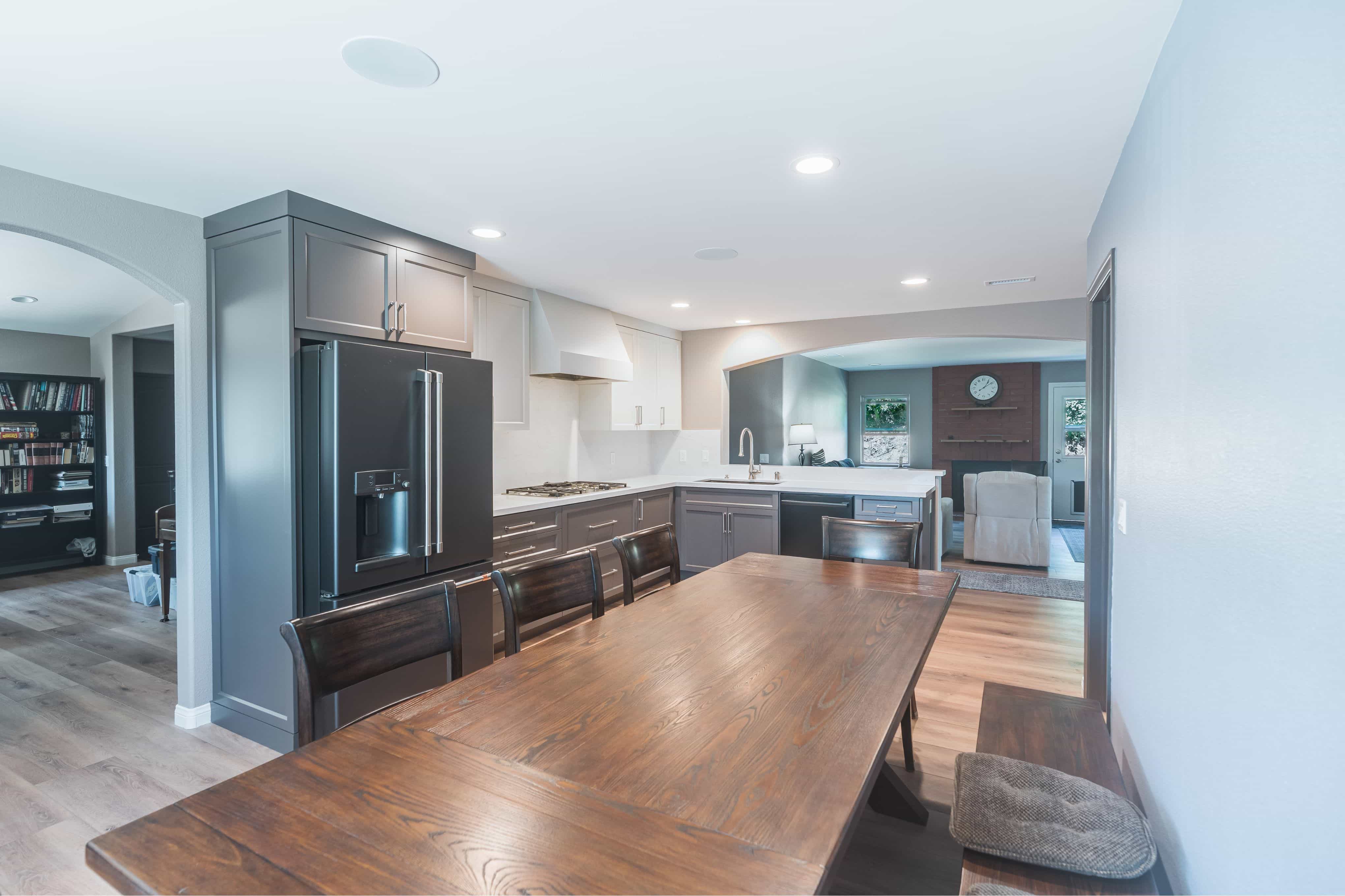 Open kitchen and dining area with gray and white shaker cabinets, full-height quartz backsplash, LVP flooring and arched openings