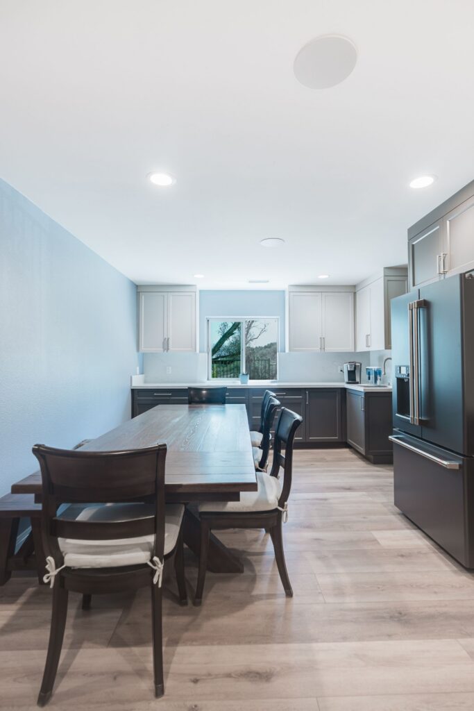 Dining area beside a kitchen with gray lower and white upper shaker cabinets, quartz backsplash, window and LVP flooring