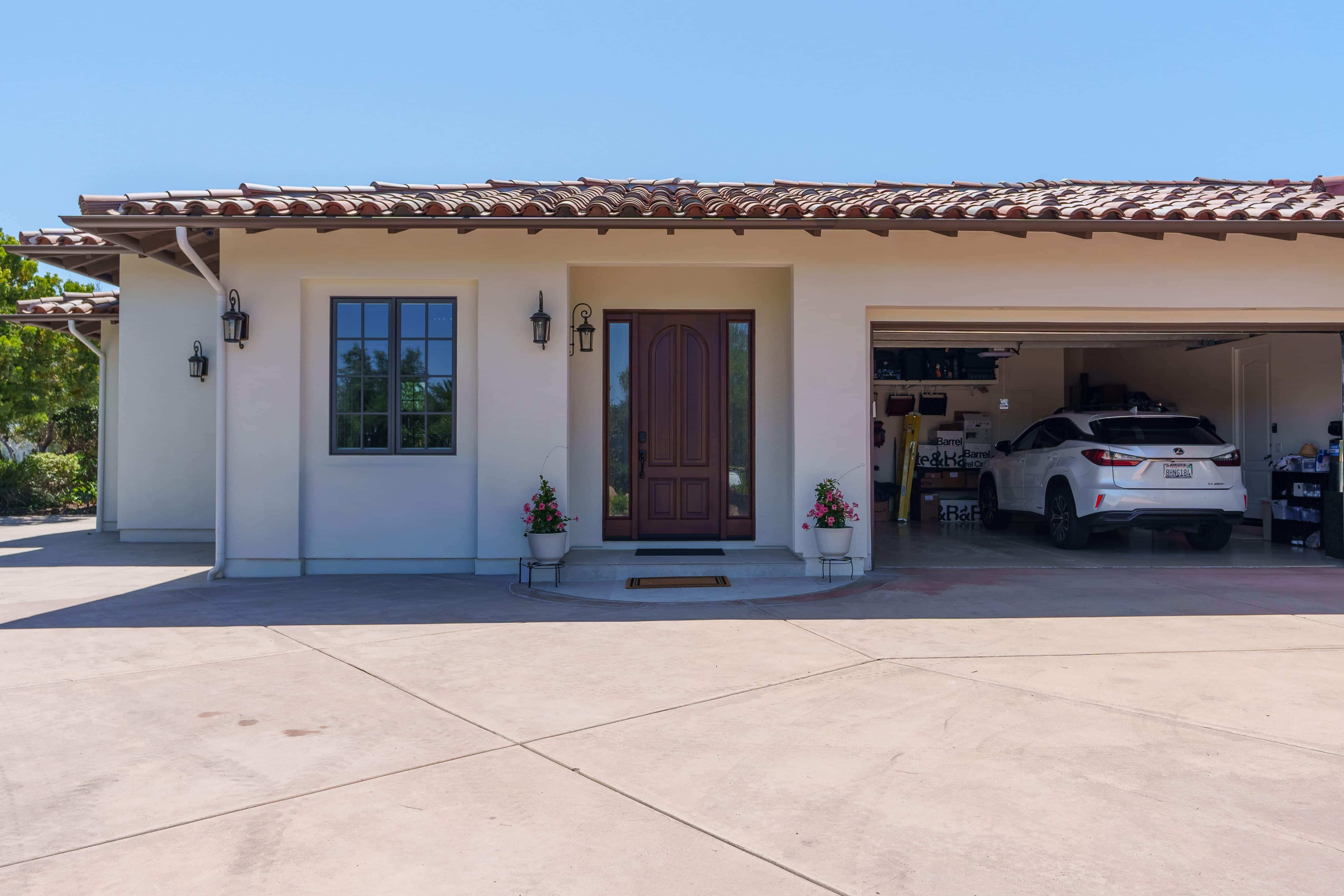 Stucco exterior with clay tile roof, wood entry door with sidelights, lantern sconces and a concrete driveway