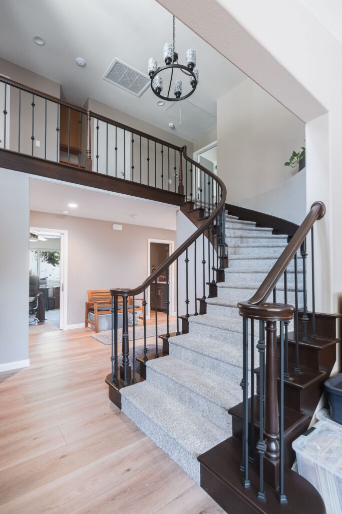 Overhead view of a curved staircase with carpeted treads, dark wood stringers, iron balusters and a cylinder-shade chandelier