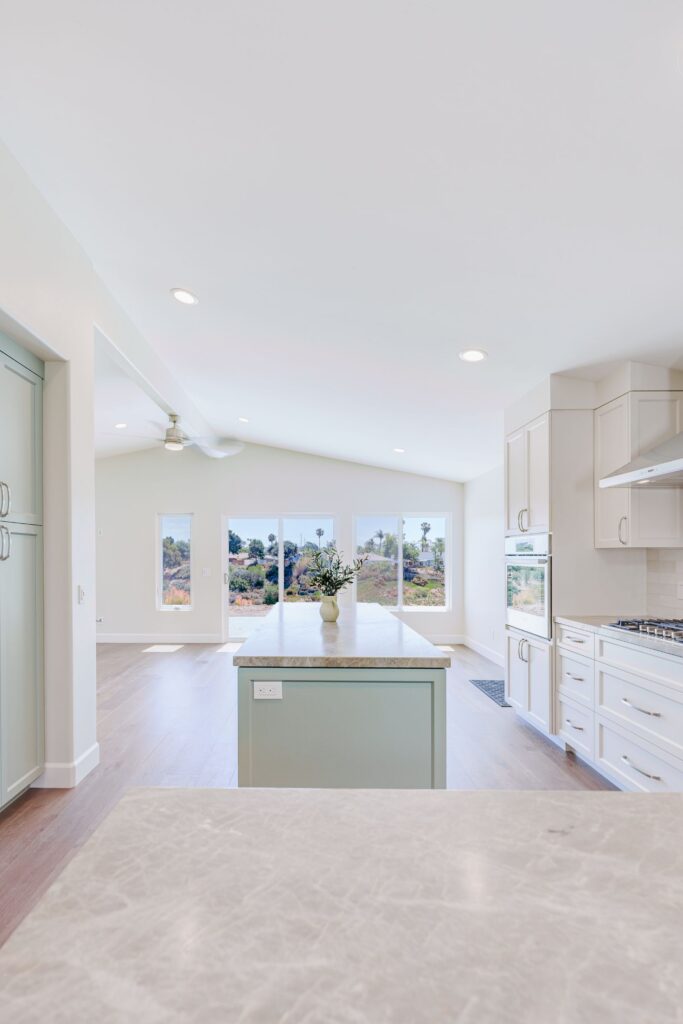 Sage green island centered on a sliding glass door and windows beneath the vaulted ceiling of the open kitchen