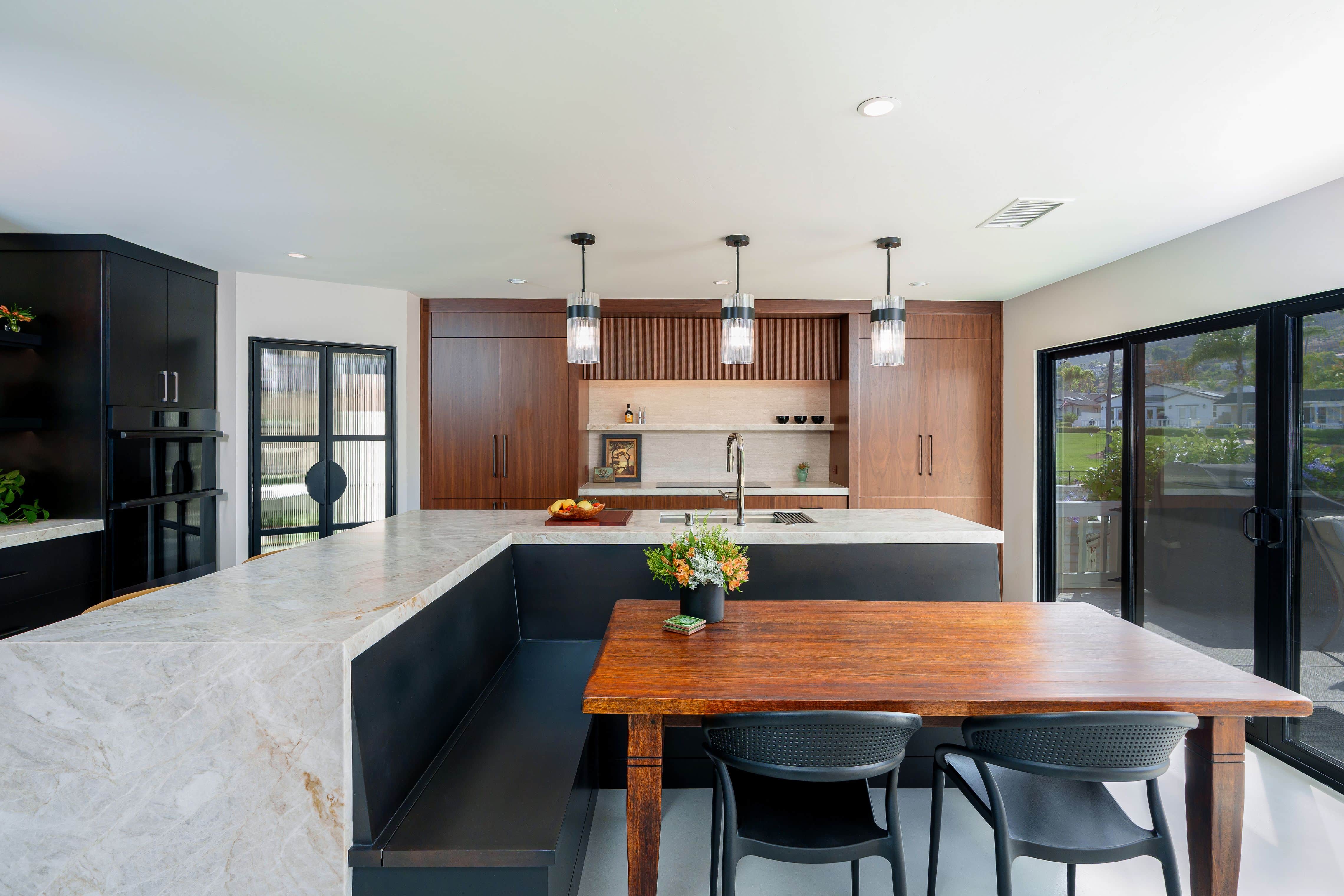 Walnut cabinet wall with induction cooktop, fluted hood panel, stone backsplash and floating shelf beside a quartzite island