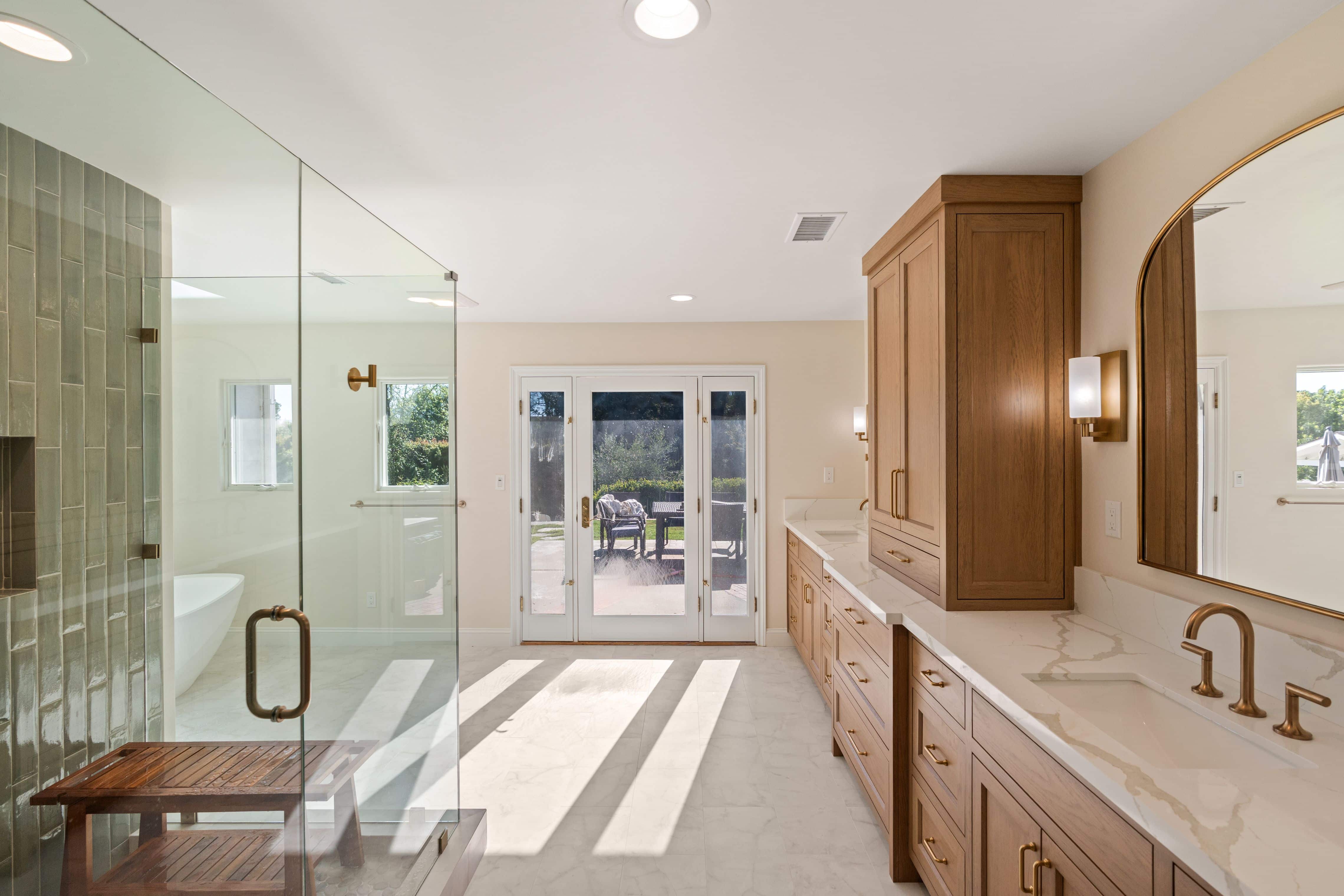 Primary bath with frameless glass shower, wood double vanity with tower cabinet and French door with sidelites to patio