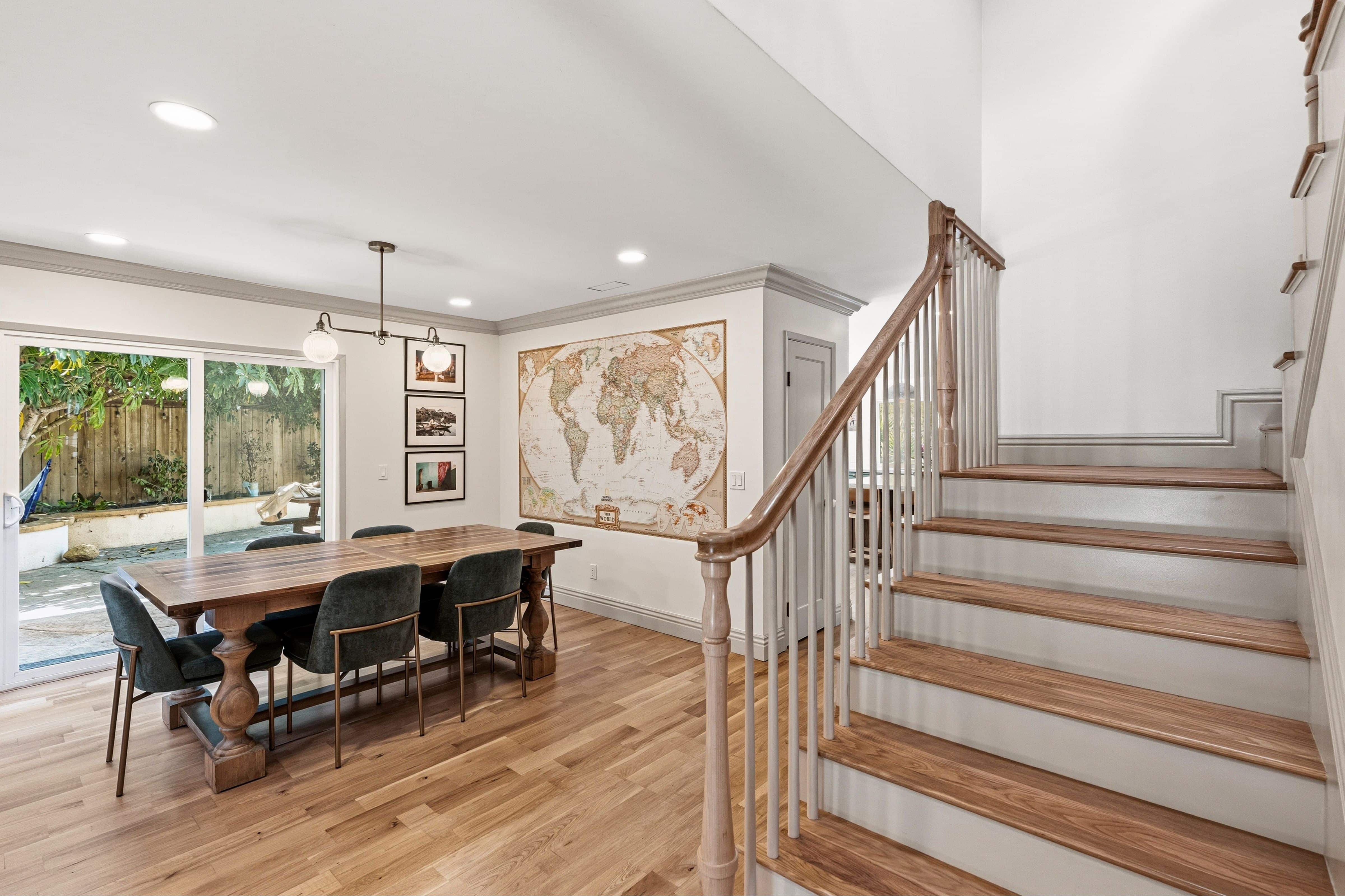 Dining room with sliding door to patio, globe pendant and hardwood floors beside a staircase with wood treads and handrail