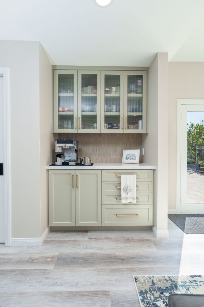 Built-in coffee bar with sage green cabinets, reeded glass upper doors, wood-look hexagon tile backsplash and brass pulls