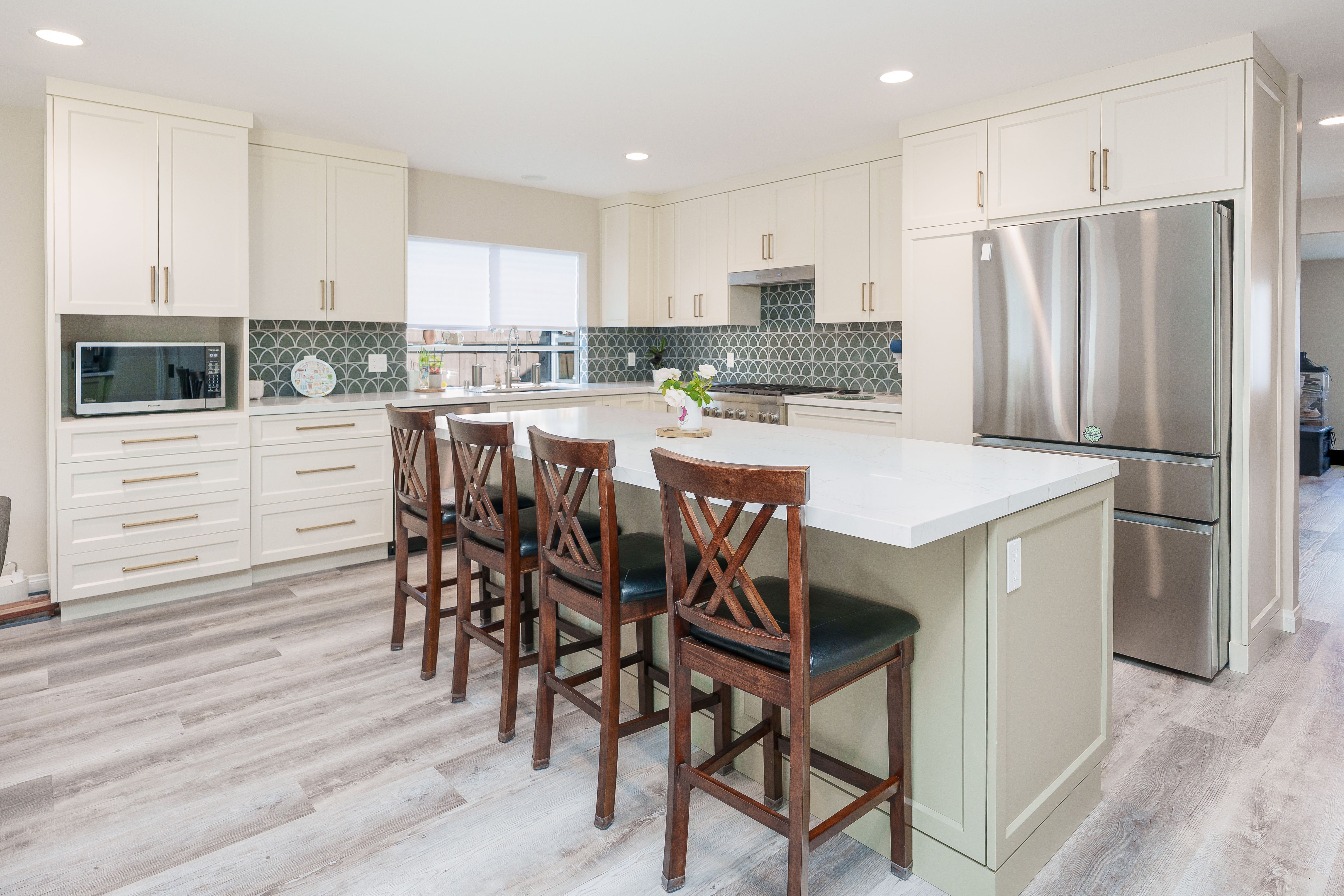 Open kitchen with sage green island, white countertop, four wood barstools, microwave niche and gray LVP flooring