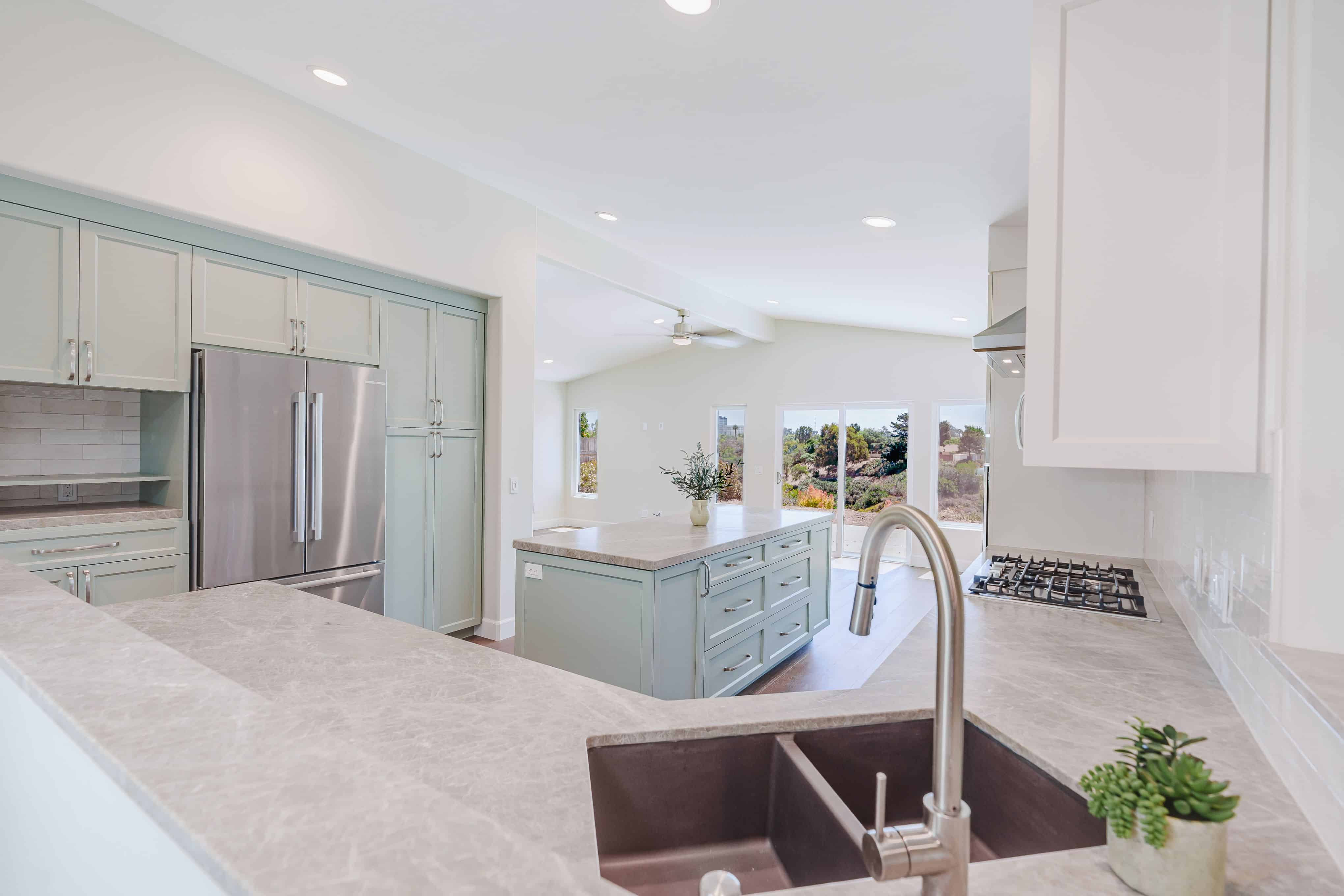 Kitchen with a double-bowl sink, sage green island, built-in refrigerator flanked by pantry cabinets and an open appliance nook