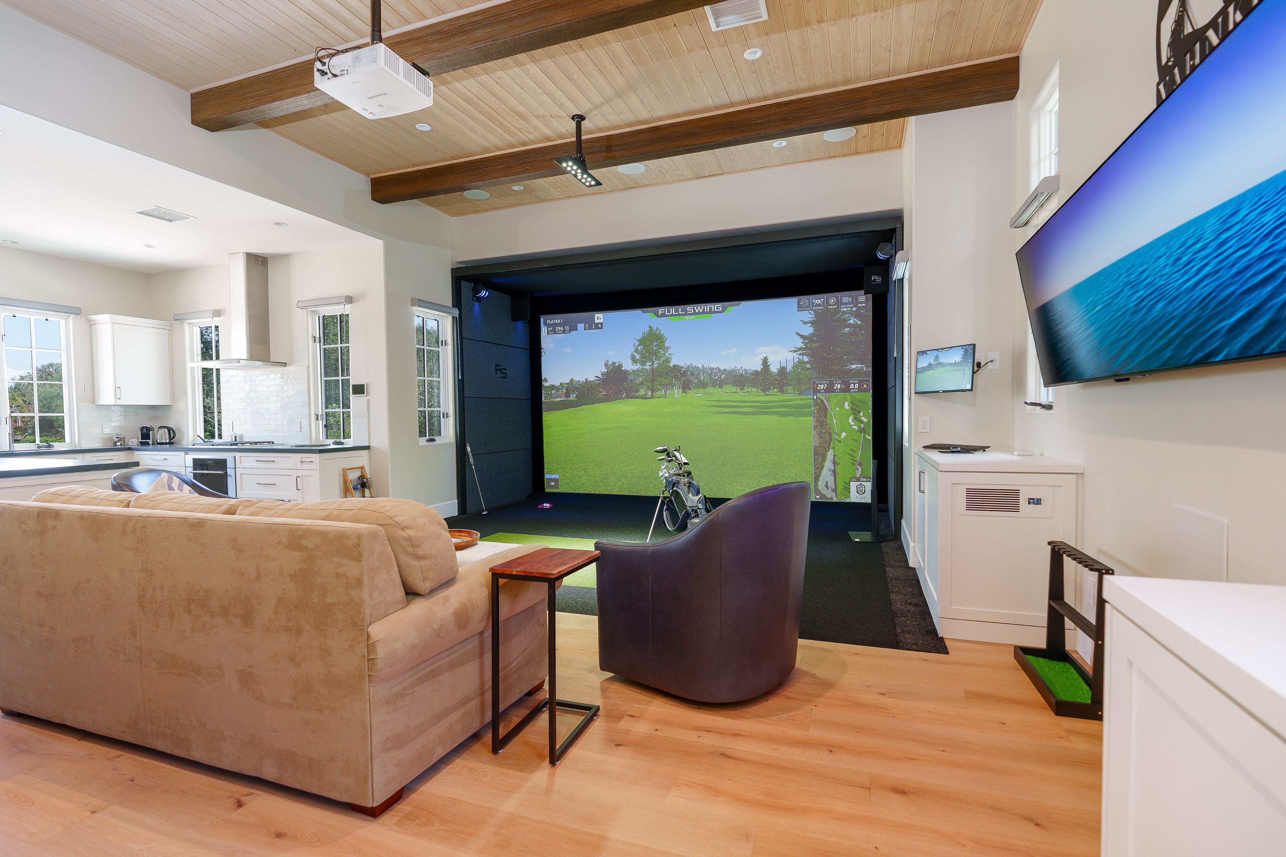 Great room with golf simulator bay, wood plank ceiling with dark beams, wide-plank wood floors and an open kitchen