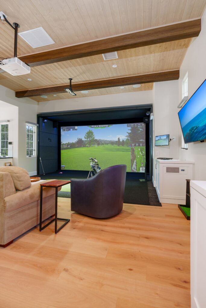 Golf simulator bay with a turf hitting area, beamed wood plank ceiling, ceiling projector, wall TV and club rack