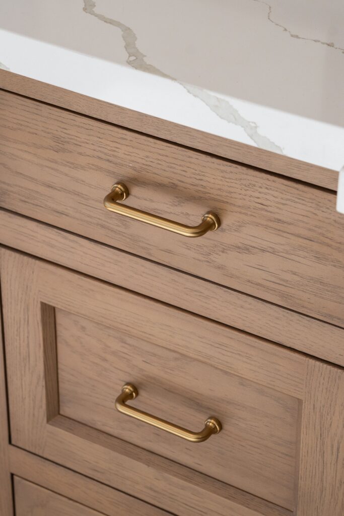 Close-up of inset wood vanity drawers with gold-tone pulls below a white quartz countertop with gold veining