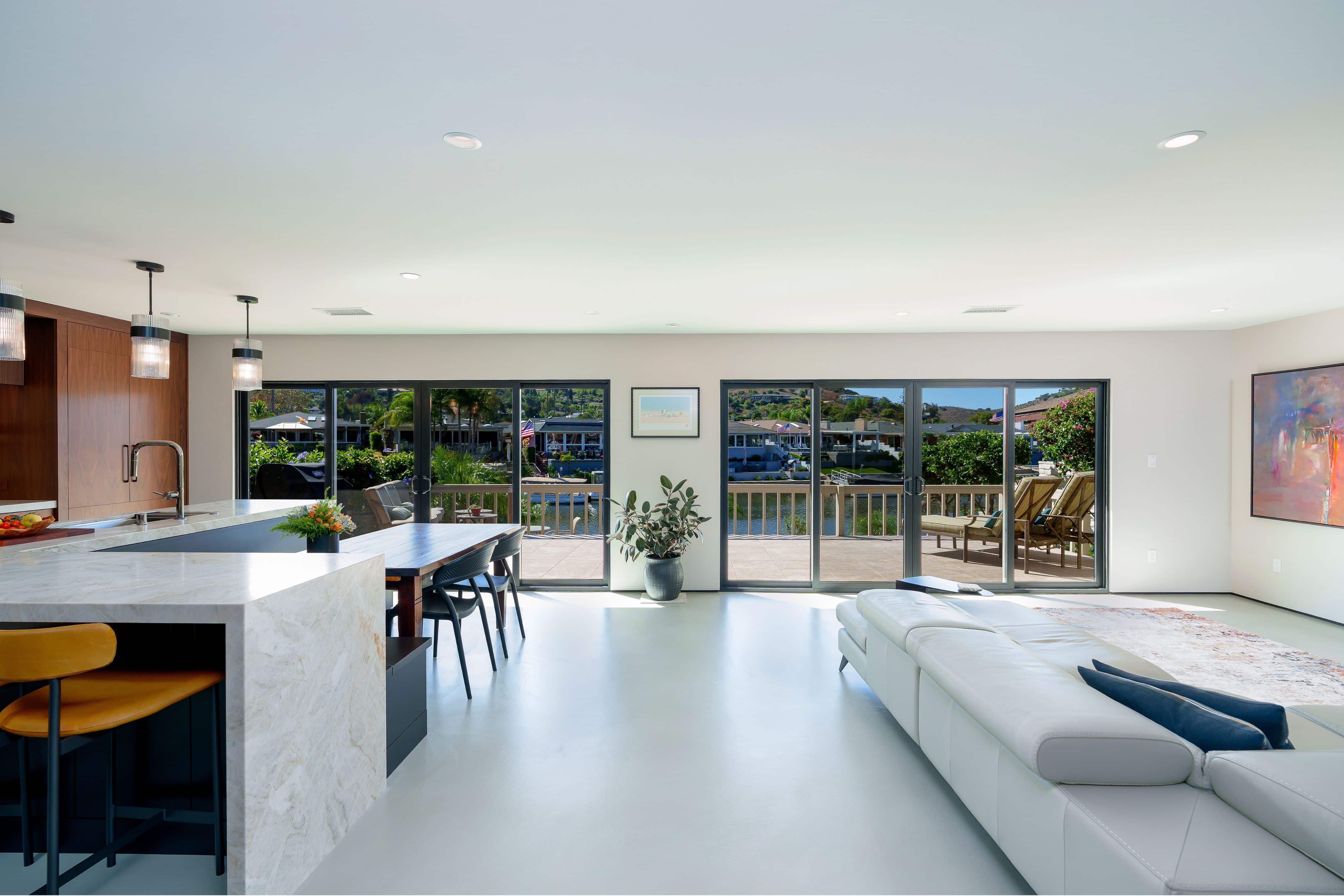 Kitchen with waterfall quartzite island, built-in black banquette, wood dining table, glass pendants and black sliding doors