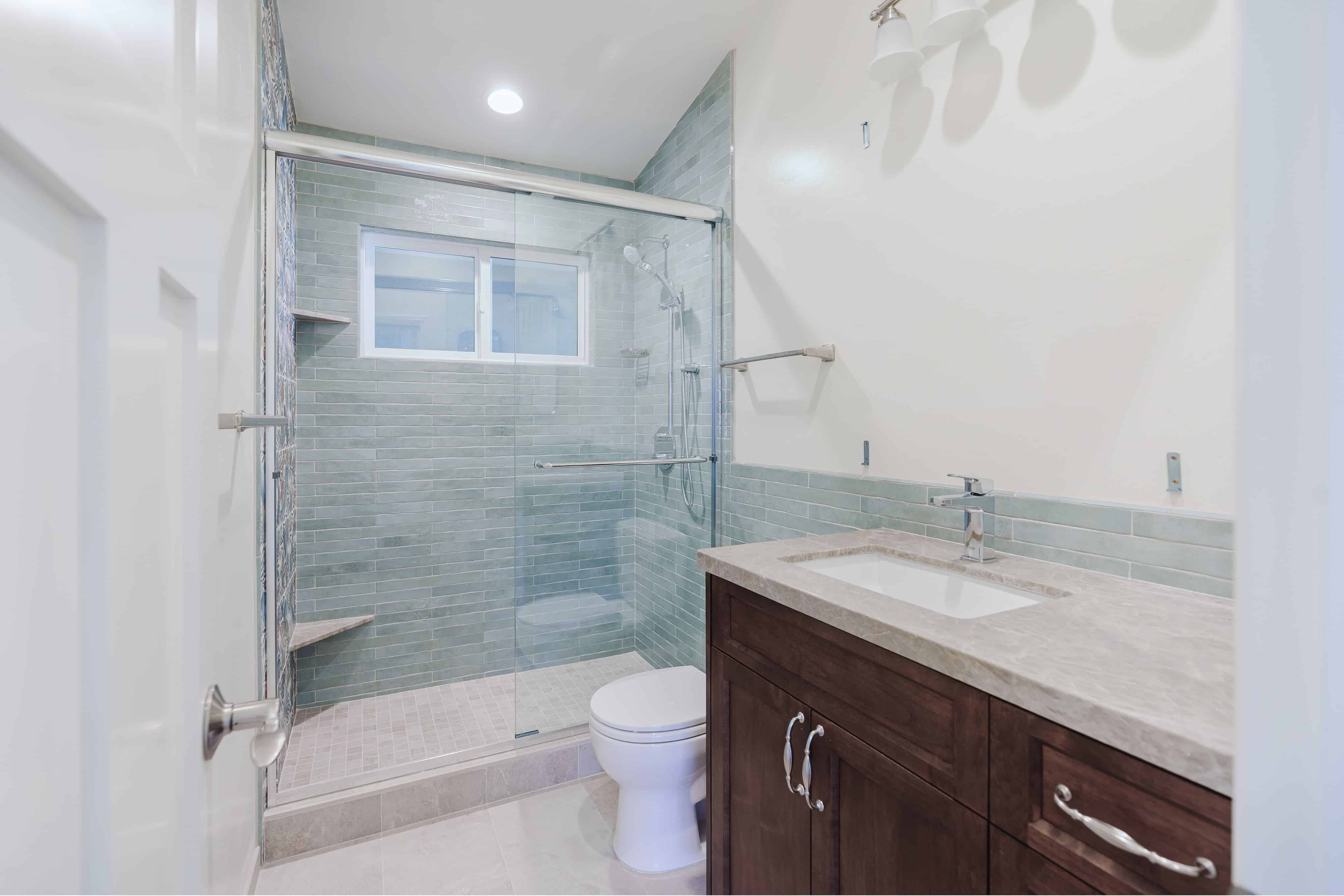 Bathroom with a glass-enclosed walk-in shower, sage green tile, patterned accent wall and dark wood Shaker vanity