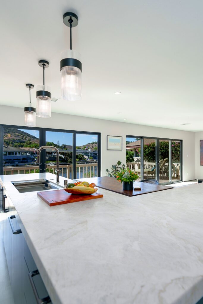 Quartzite kitchen island with stainless sink, ribbed glass pendants and black sliding doors overlooking a lake in San Marcos