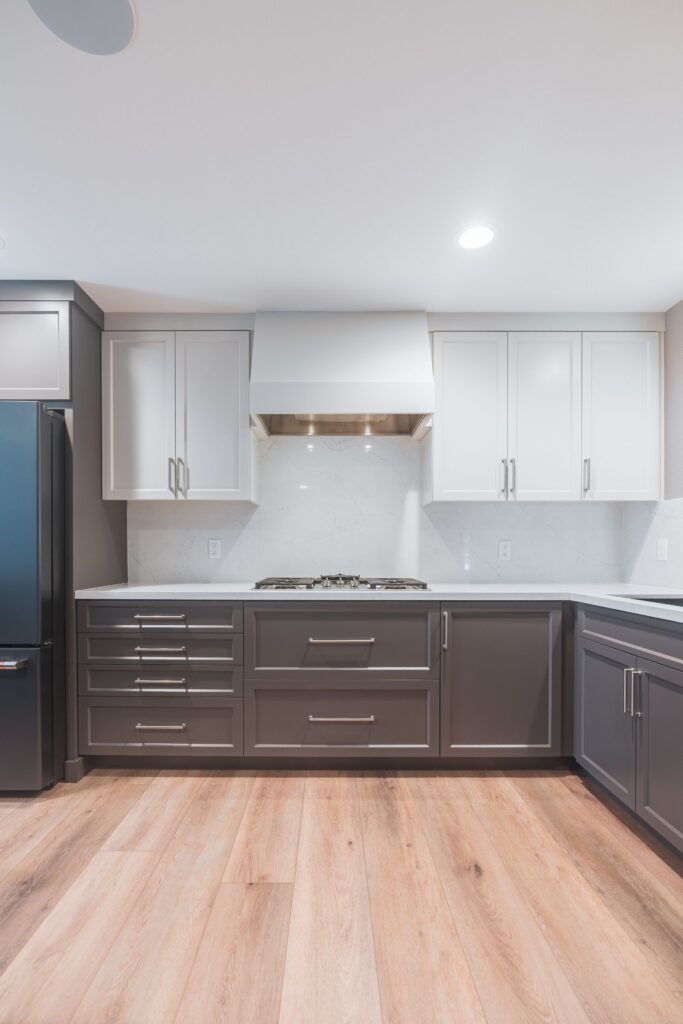 Cooktop wall with white range hood, white upper and gray lower shaker cabinets, full-height quartz backsplash and LVP floor