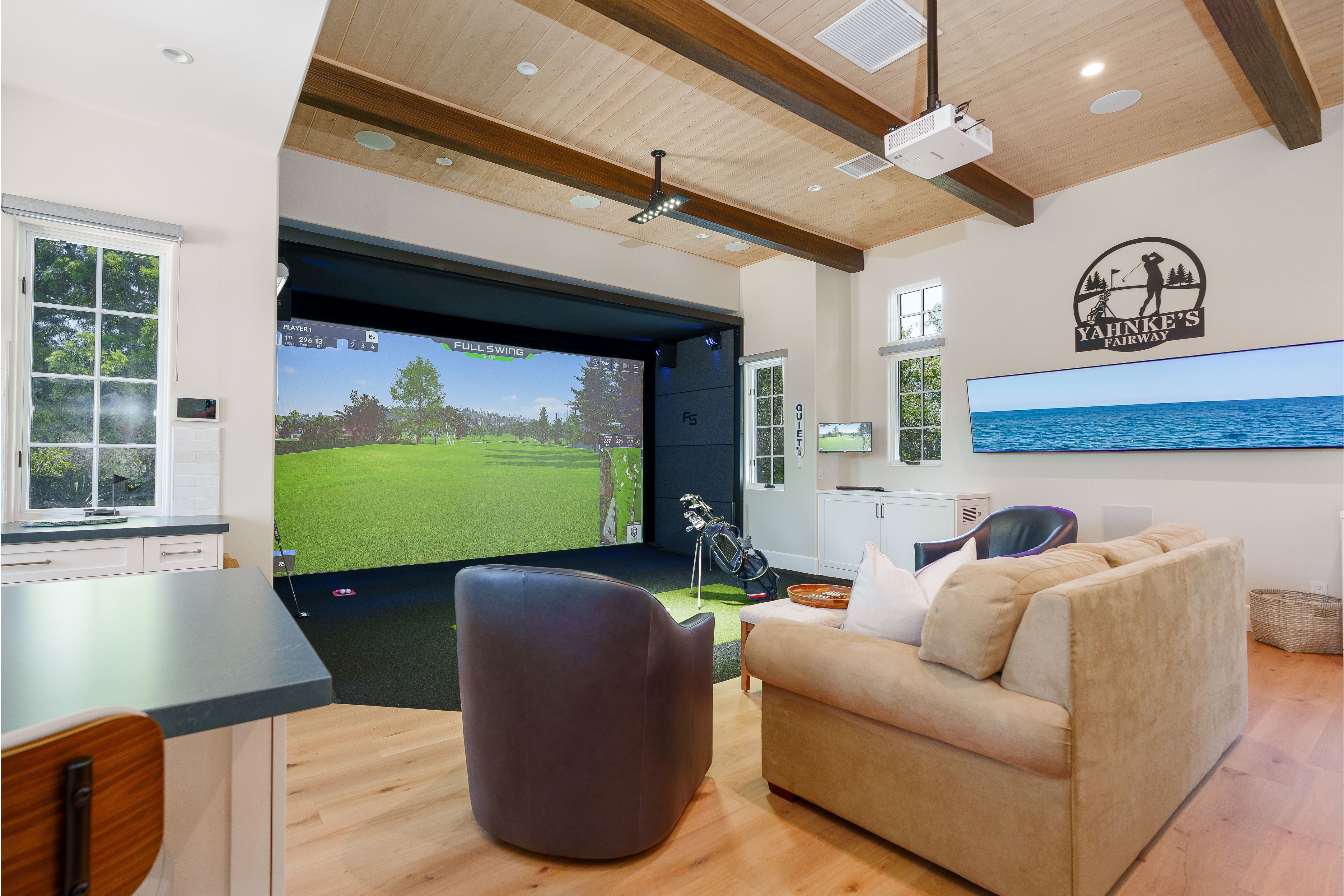 Kitchen island with gray countertop facing a golf simulator, swivel chairs, sleeper sofa and beamed wood ceiling