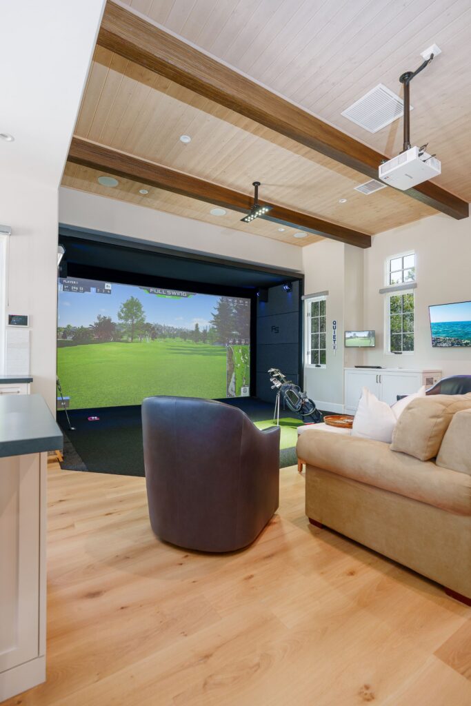 Great room with a golf simulator screen, leather swivel chair, sofa, divided-lite windows and dark wood ceiling beams