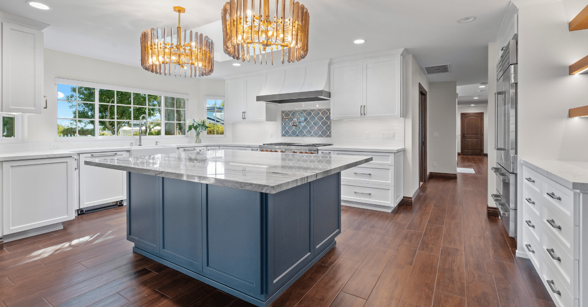 Bright remodeled kitchen with white cabinets, blue island, stone countertops, and wide open circulation.