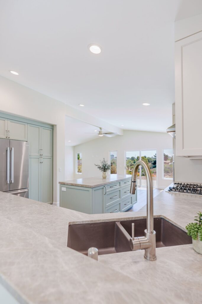 Kitchen double-bowl sink and pull-down faucet looking past a sage green island toward the living room sliding door