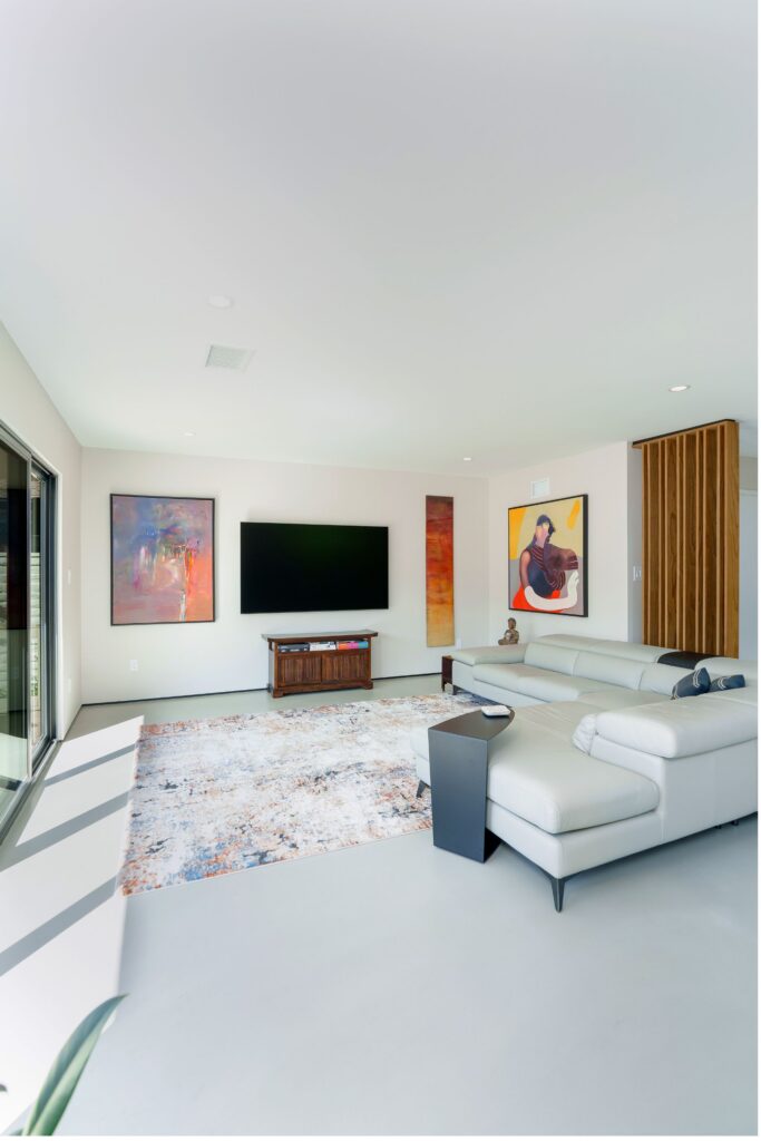 Living room with white leather sectional, wall-mounted TV, framed artwork, wood slat divider and concrete floor