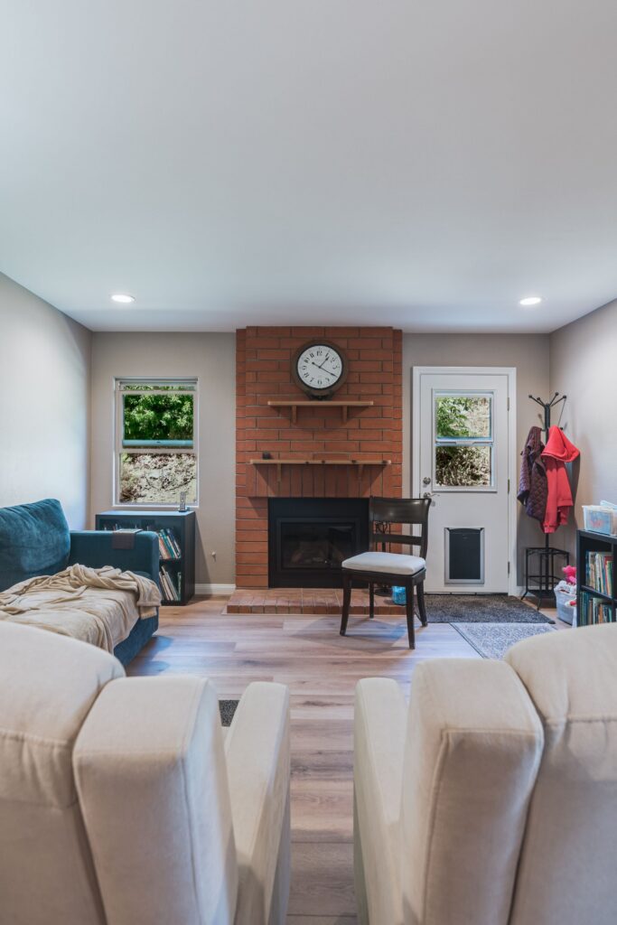 Library and den with dark wood bookcases, blue sectional, writing desk, ceiling fan and TV over a black stone fireplace