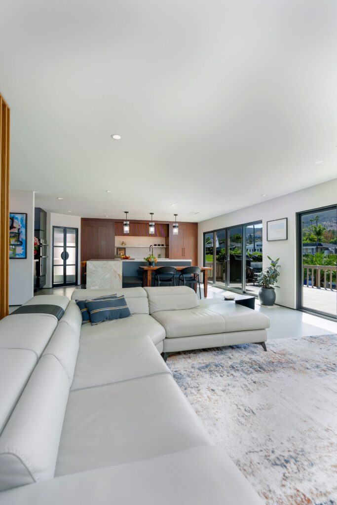 Open-concept living room and kitchen with walnut cabinetry, waterfall island, three pendants and black sliding doors