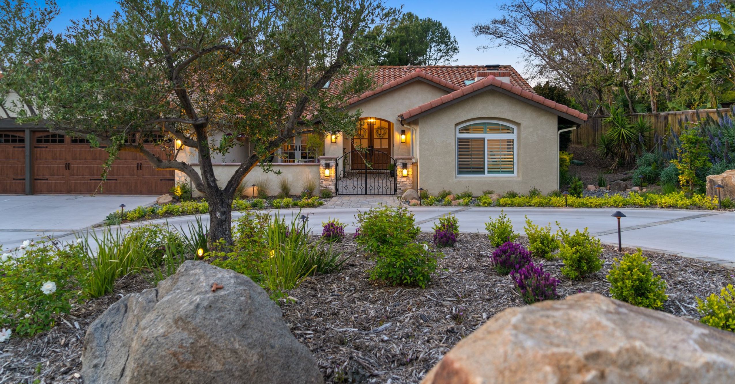 Spanish-style San Diego home with stucco exterior, red tile roof, landscaped front yard, driveway, and illuminated entry.
