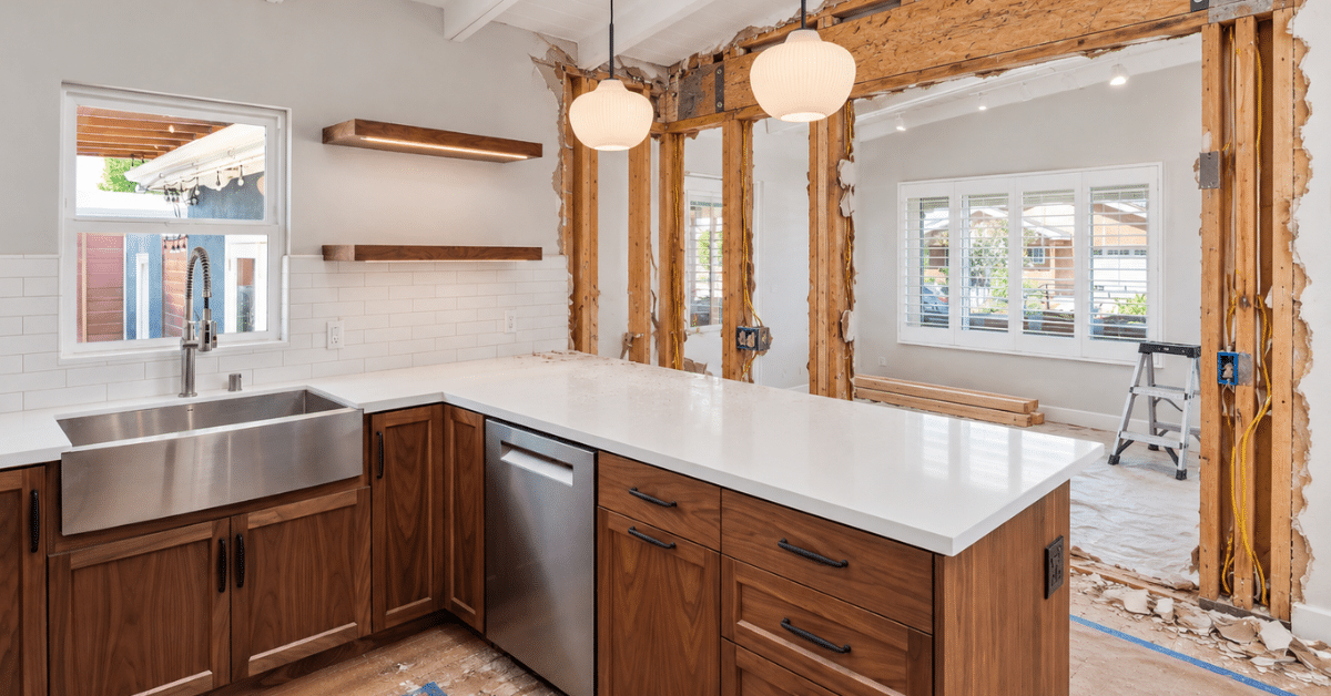 Kitchen remodel in progress with exposed wall framing beside a large island and white countertops.