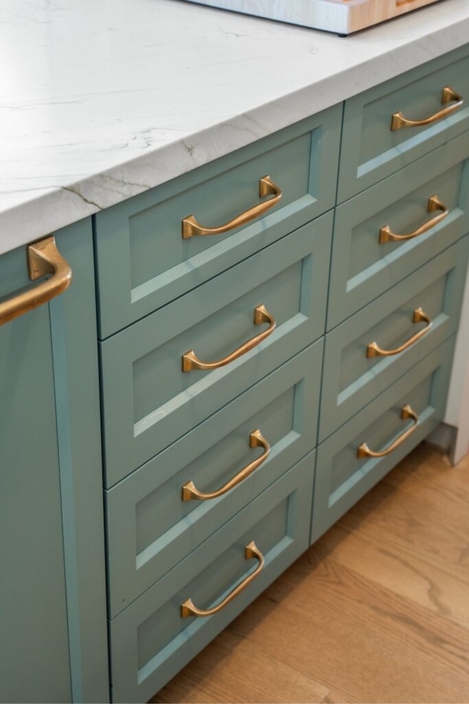 Kitchen island with six upholstered stools, concrete dome pendants, a flush cooktop and green perimeter cabinetry
