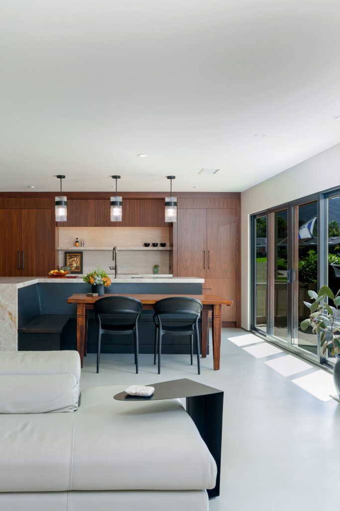 Built-in black banquette at quartzite waterfall island with wood dining table, walnut cabinets and sunlit sliders
