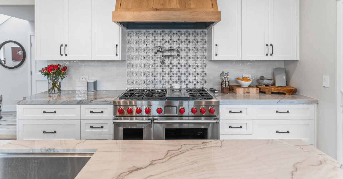 White kitchen cabinetry with professional stainless steel range, patterned backsplash, and stone countertops.