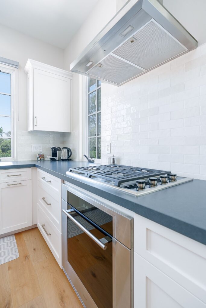 U-shaped ADU kitchen with white shaker cabinets, dark countertops, a window over the sink and a stainless range hood
